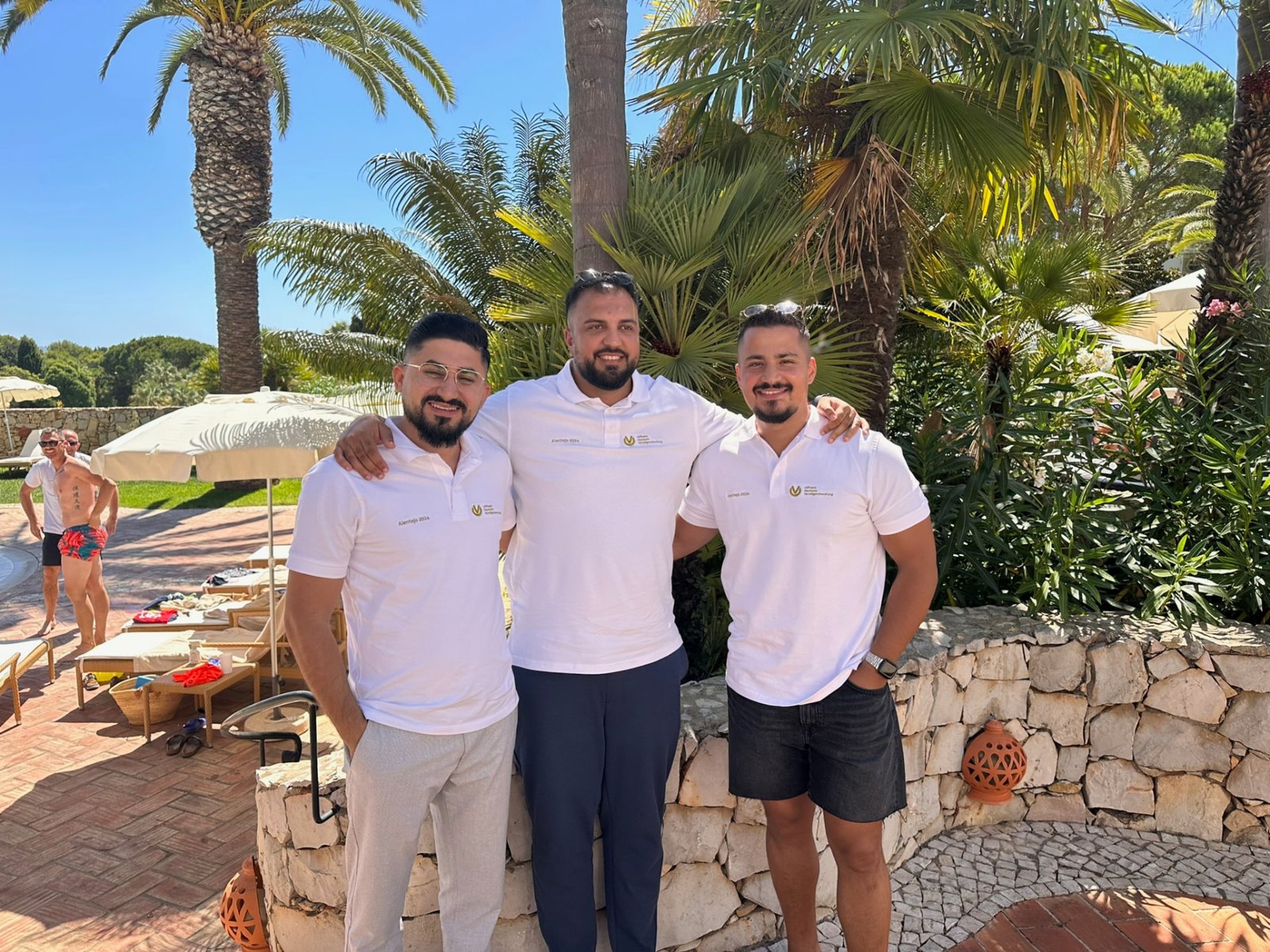Farshad Sahab mit zwei Kollegen an einer Poolanlage mit Palmen im Süden